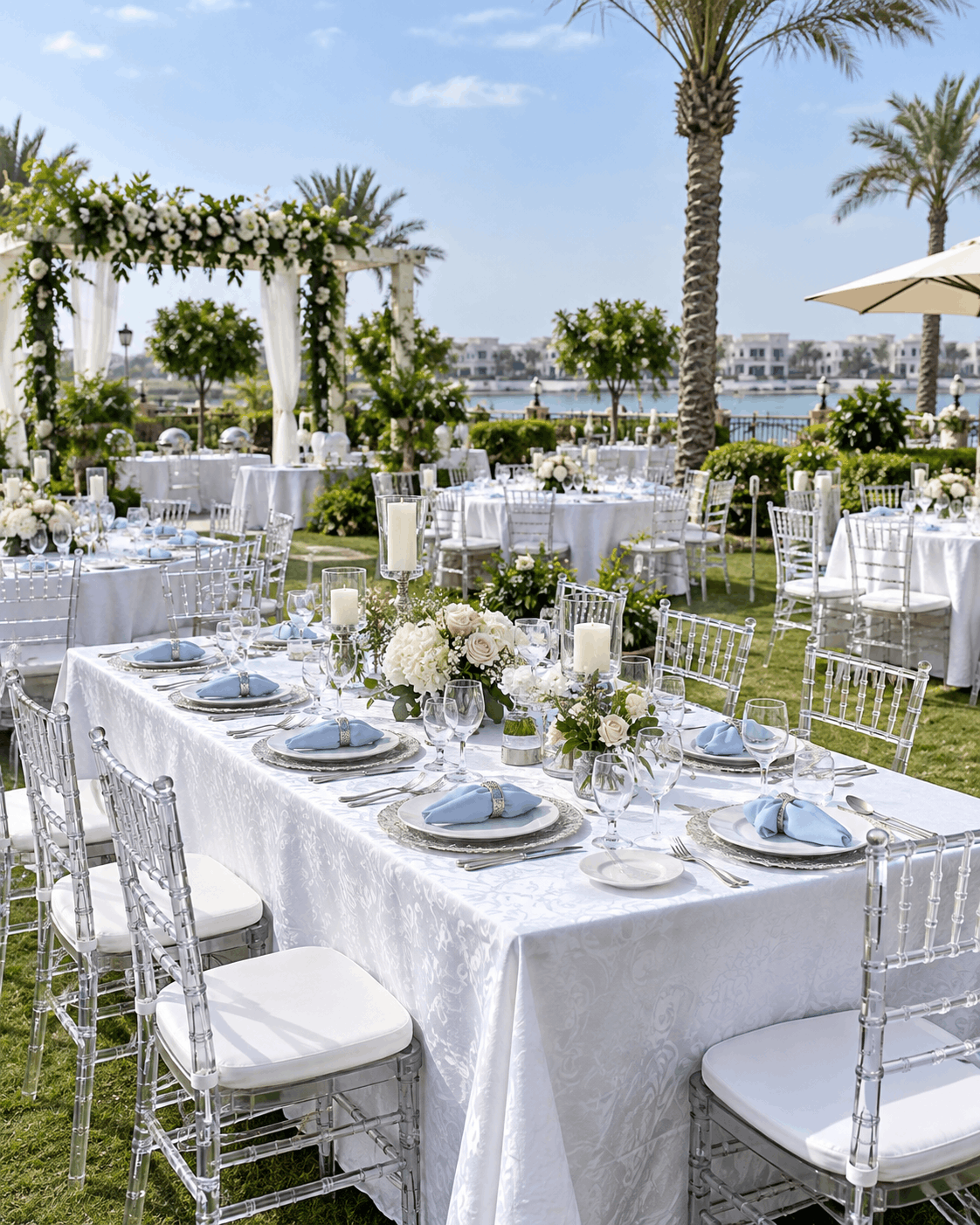 Banquet tables dressed in white linen, crystal and flowers set for an outdoor event beside the water